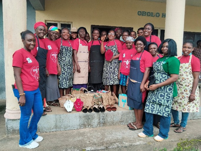 Group of women standing around plam tree crafts facing the camera.