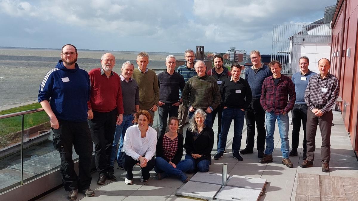Group of people standing and kneeling in 2 rows on roof top with sea in background.