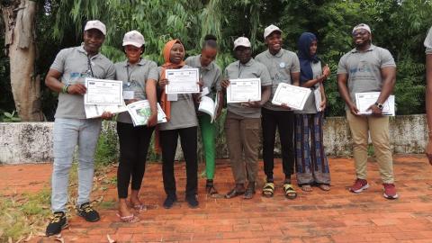 Group of young people standing in row, each holding up a sheet of paper, facing the camera.