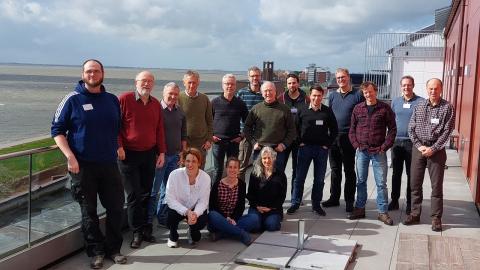 Group of people standing and kneeling in 2 rows on roof top with sea in background.